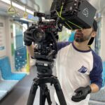 Camera operator filming video content on a train, focused on capturing dynamic footage.